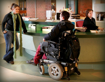 Woman speaking to student in wheelchair in college lobby.