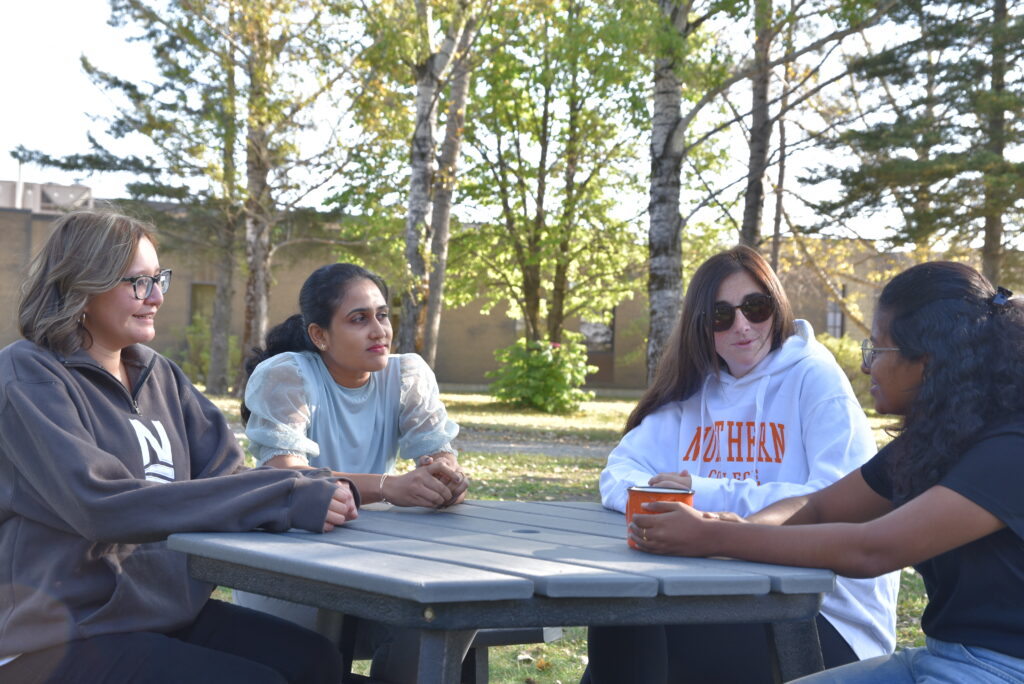 four students sitting around picnic table outside